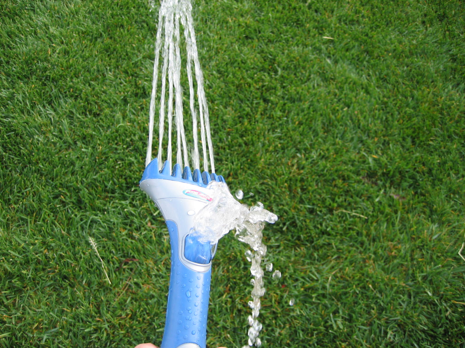 Blue and gray watering wand spraying multiple thin streams of water upward over a green lawn